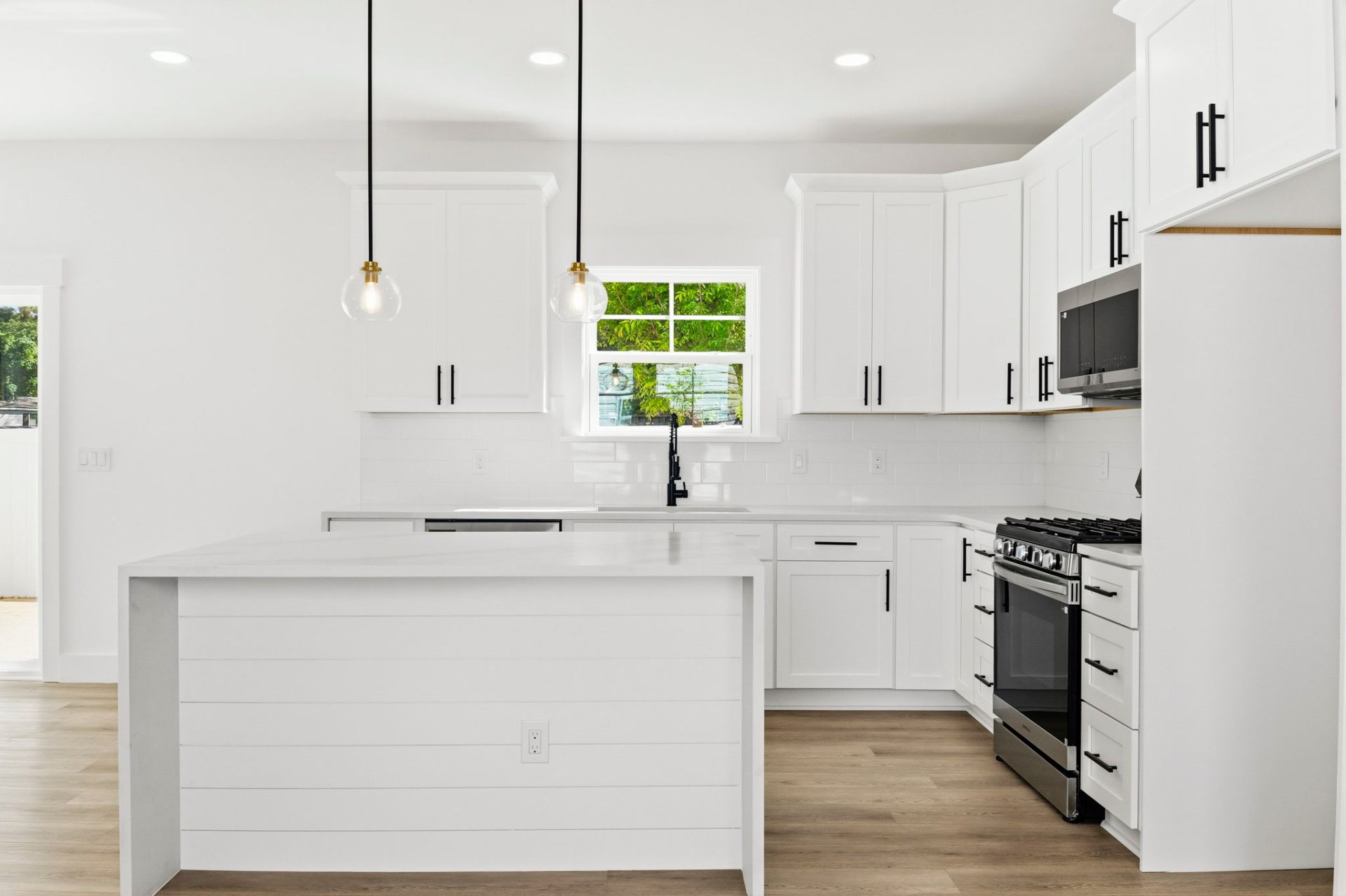 Quartz waterfall island kitchen with shaker style cabinetry and black metal finishes